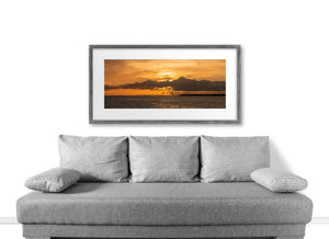 Warm orange sky and a long bridge stretch across a wide coastal sunset photograph.