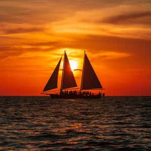 Sailing vessel crossing ocean during orange sunset
