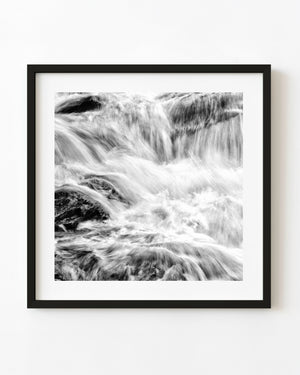 White flowing water cascades over dark rocks in a black and white abstract waterfall photograph.