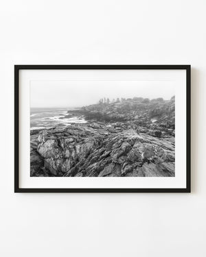 Fog softens the rocky Portland, Maine coastline above white surf in a black and white photograph.