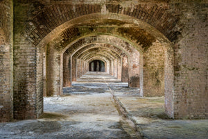 A long Fort Jefferson corridor with aged brick pillars, curved arches and a worn stone floor.