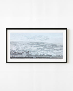 Fractured Antarctic snow cliffs rise above dark polar water dotted with small pieces of ice.