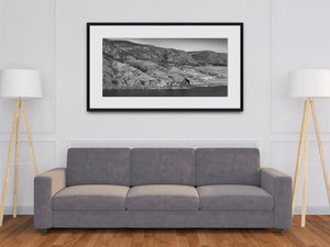 Black and white photograph of a train winding along the base of rocky slopes