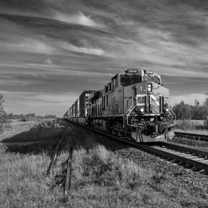 Black and white freight train photograph beneath sweeping prairie clouds in Saskatchewan