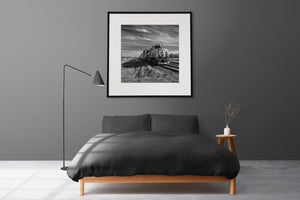 Square monochrome photograph of a locomotive and receding freight cars on prairie tracks