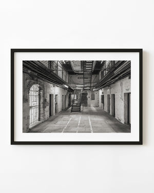 A central staircase rises between cell doors inside Fremantle Prison in black and white