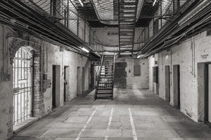 Black and white interior of Fremantle Prison with cell doors and overhead safety netting