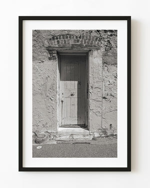 A weathered wooden cell door sits in rough stonework at Fremantle Prison in black and white