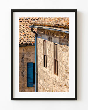 Warm stone walls and tall windows beside a blue shutter on a French house