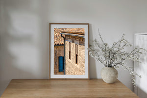 A blue wooden shutter contrasts with warm stone walls beneath terracotta roof tiles