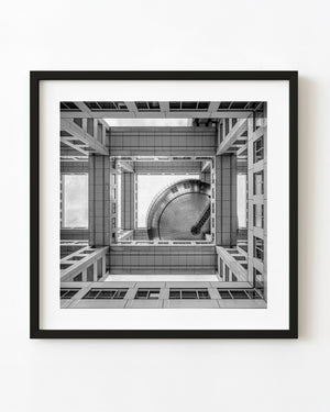 An upward black and white view of the Fuji TV building with geometric beams and a large metal sphere