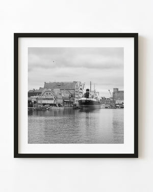 A docked ship stands beside gabled waterfront buildings in Gdańsk in a black and white harbor photograph