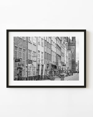 Historic Gdańsk façades and stone entrance steps lead toward a brick tower in a monochrome street photograph