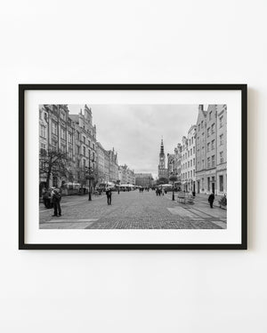 People walk along Gdańsk’s cobblestone main street toward a clock tower in a black and white November photograph