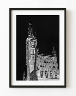 Gdańsk Main Town Hall’s illuminated clock tower rises against a dark sky in black and white