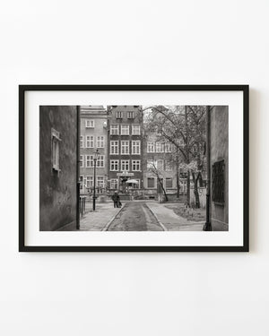 A narrow Gdańsk laneway leads toward historic gabled façades in a black and white photograph