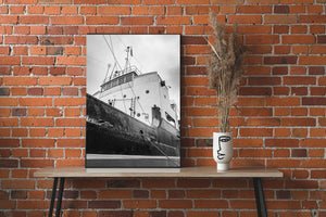 A weathered steel hull fills the foreground beneath a ship’s white bridge and cloudy sky