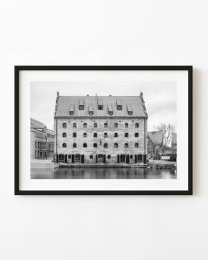 A historic brick waterfront building with arched windows stands beside water in Gdańsk in black and white