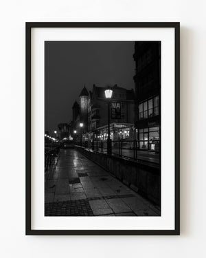 Glowing streetlamps line a wet Gdańsk waterfront walkway in a black and white night photograph