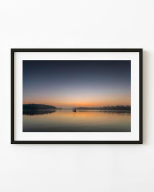 A sailboat reflects on calm Georgia water beneath a peach and blue sunrise sky