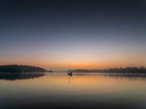 Sailboat reflected on calm coastal water at dawn