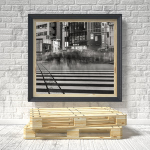 Framed black and white cityscape print on a brick wall with a wooden pallet at the bottom.