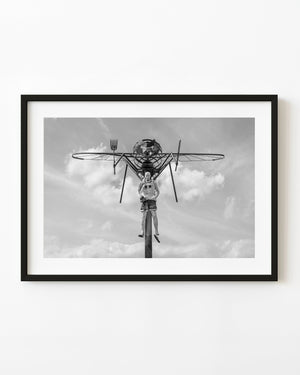 A giant mosquito sculpture holds a human figure beneath a cloudy Ontario sky in black and white