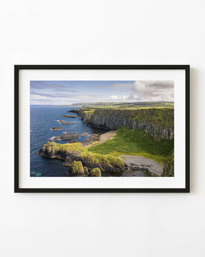 Green cliffs curve above blue water along the Giant’s Causeway coastline in Northern Ireland