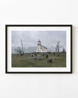 Gimsøy’s white wooden church stands beside a graveyard and snowy coastal mountains in Norway