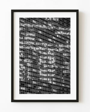 Illuminated windows form a grid across a glass office building at night in black and white