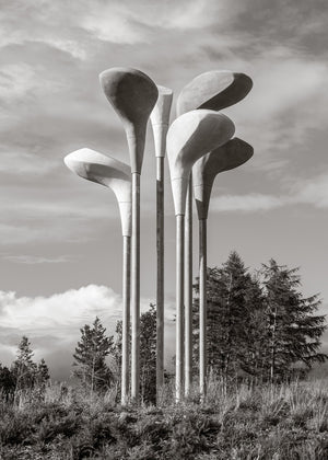 A group of oversized golf club heads stands on slender poles beneath a cloudy Scottish sky