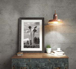 Monochrome outdoor sculpture photograph with oversized golf club heads and textured clouds