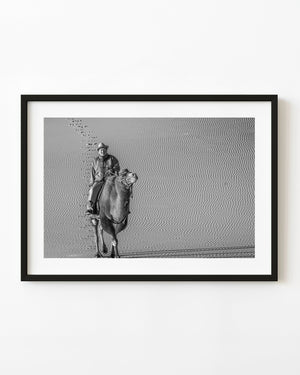 A camel rider crosses rippled Gobi Desert sand in a black and white photograph