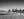 Three double-humped camels follow a herder across rippled desert sand