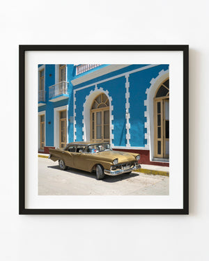 A golden classic car is parked against a vivid blue facade in Trinidad, Cuba