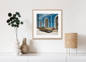 White balconies and arched doors rise above a gold vintage car in Cuba