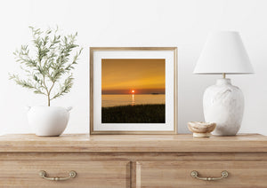 Dark grasses frame a peaceful Canadian lake sunset with golden reflections