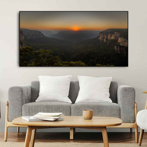 The small rising sun shines between distant ridges in the Blue Mountains
