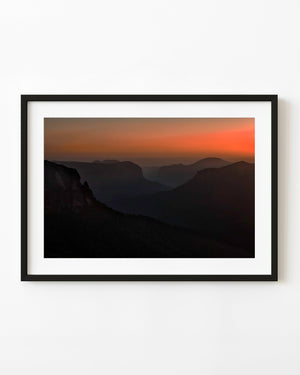 Orange dawn light glows above shadowed cliffs at Govetts Leap lookout in the Blue Mountains
