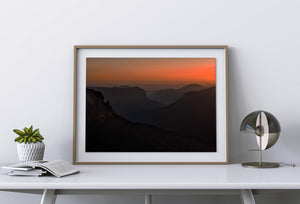 Forested slopes and distant ridges form dark silhouettes beneath a glowing horizon