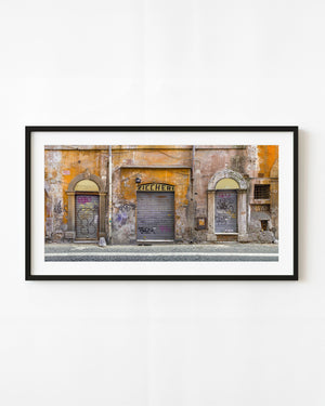 Graffiti-covered shop shutters line a weathered orange wall in Rome