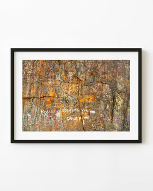 Painted graffiti marks a weathered orange and grey rock face in Maine