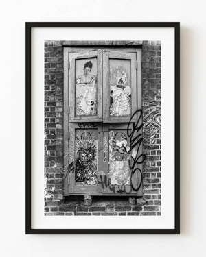 Graffiti and pasted portraits cover a weathered London window in a monochrome photograph