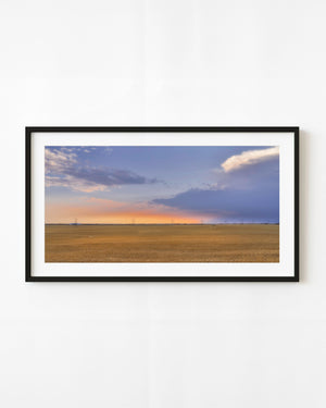 A grain train crosses the Saskatchewan horizon beneath a glowing prairie sunset