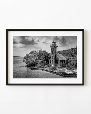 Grand Island East Channel Lighthouse stands beside Lake Superior beneath clouds in black and white