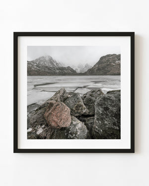 Granite boulders line a frozen Norwegian lake beneath snowy mountain peaks
