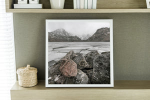A square winter landscape photograph shows granite rocks beside a frozen lake