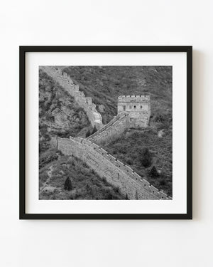 The Great Wall winds toward a stone watchtower across rugged hills in black and white