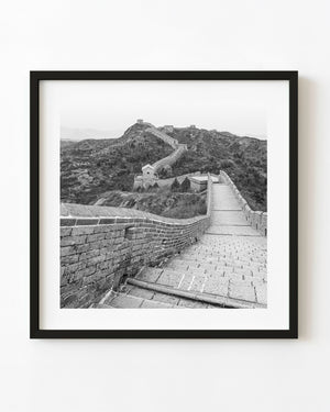 Stone steps descend along the Great Wall toward mountain watchtowers in black and white