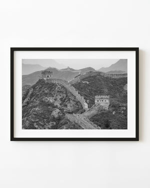 Two Great Wall watchtowers rise above rocky slopes and hazy mountain ridges in black and white